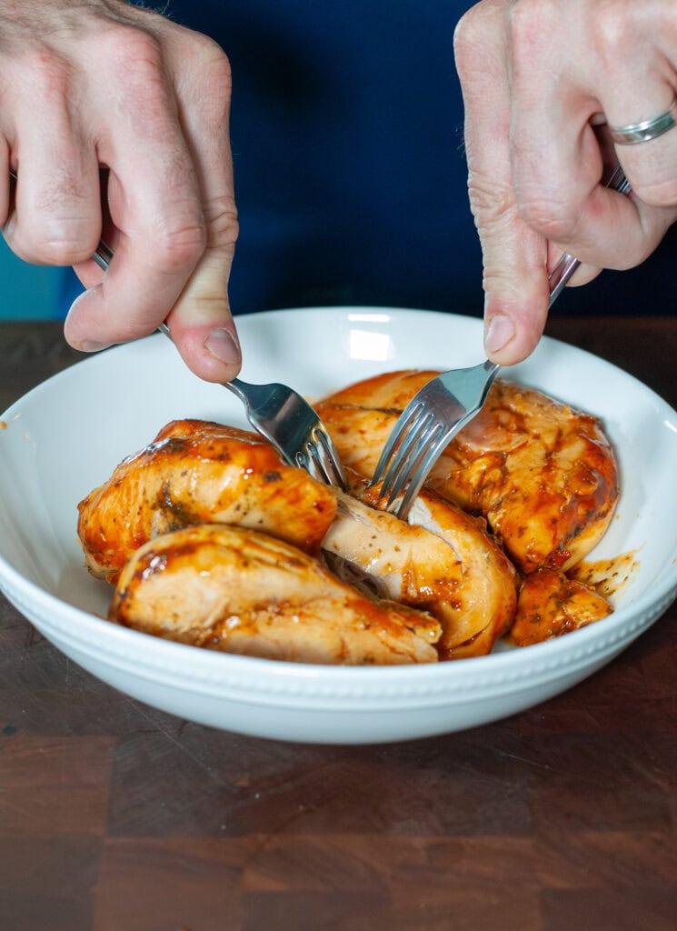 Finished chicken being shredded with two forks. 