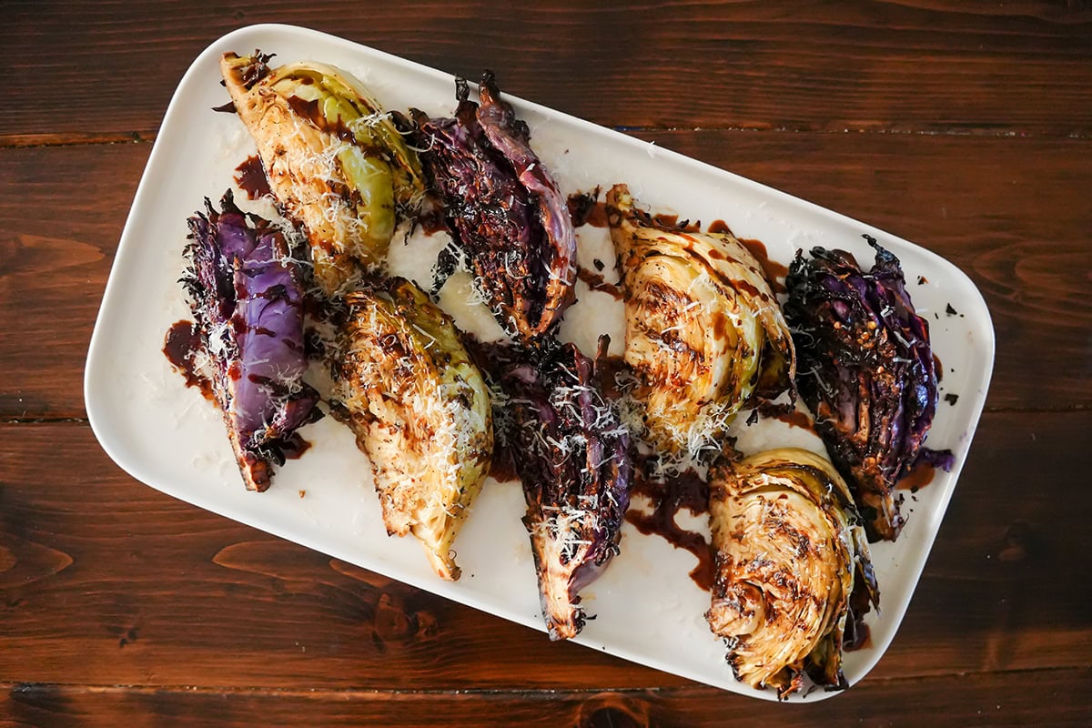 A photo of grilled cabbage steaks on a white platter. 