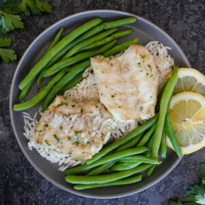 Grilled cod fish on rice with lemon slices and green beans.