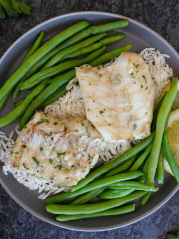 Grilled cod fish on rice with lemon slices and green beans.