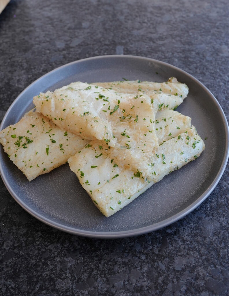 Seasoned cod filets on a plate ready to be grilled. 
