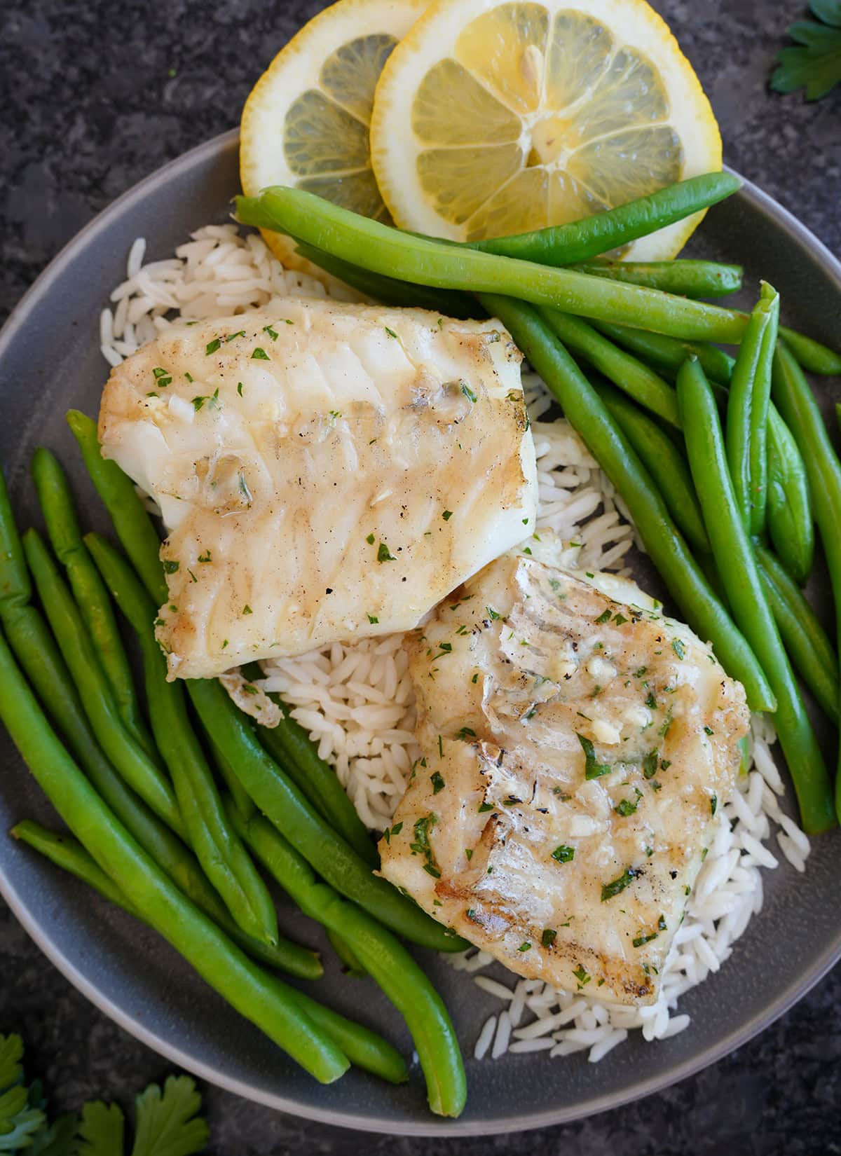 A finished plate of cod on rice served along side fresh green beans and lemon slices. 