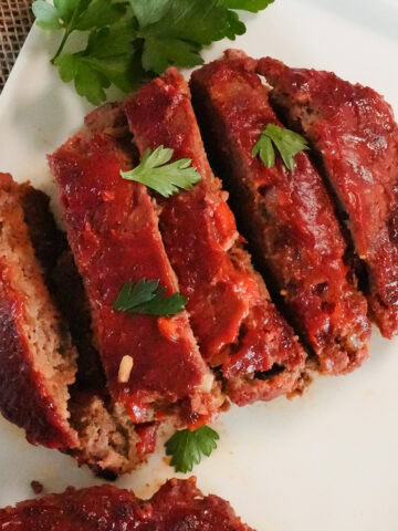 grilled meatloaf sliced into pieces on a plate with parsley.