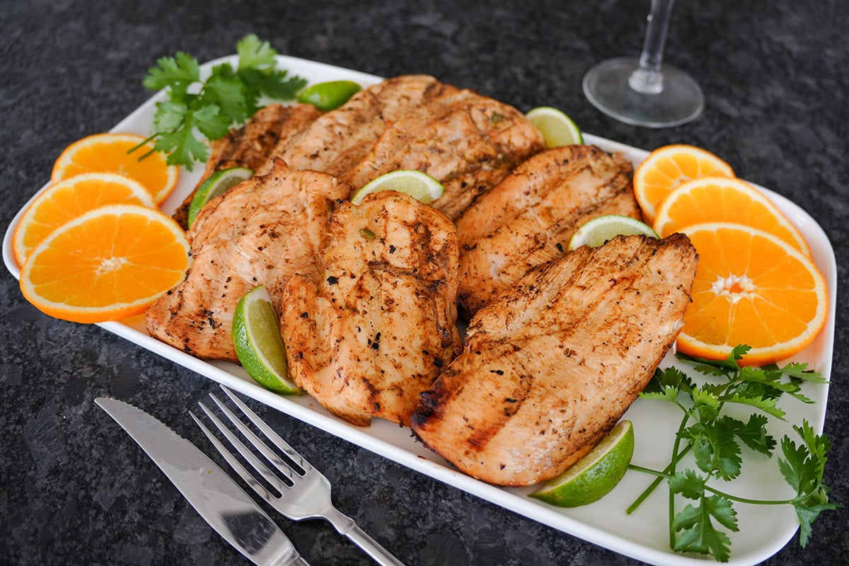 grilled chicken on a plate with orange and lime slices by a margarita.