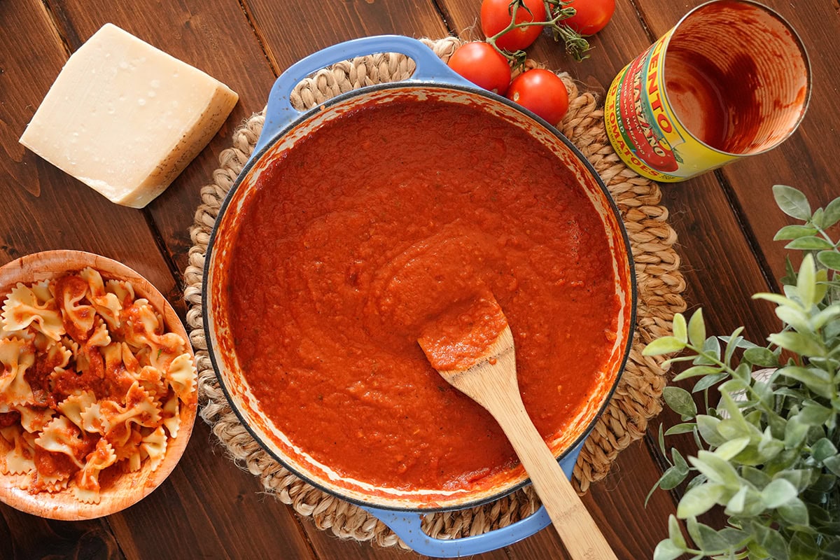 A top view of a pan of San Marzano tomato sauce with a bowl of noodles and empty tomato can. 