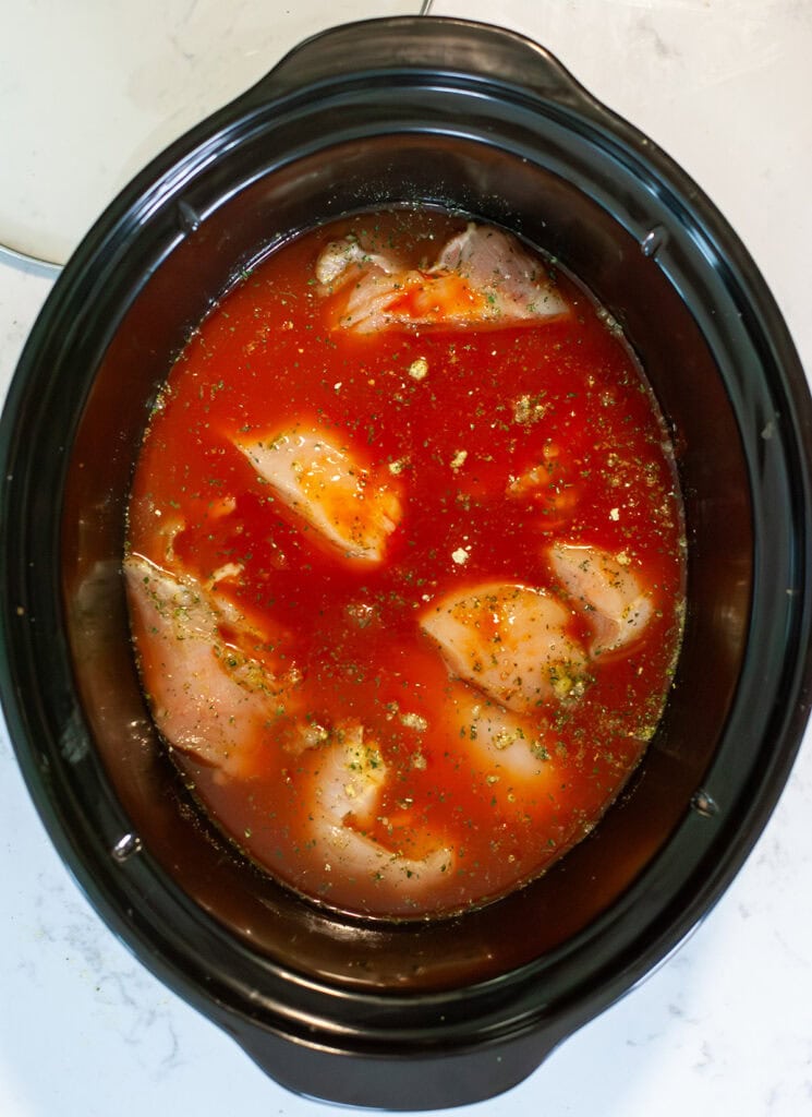 The chicken, chicken broth, and hot sauce in the crock pot ready to cook. 