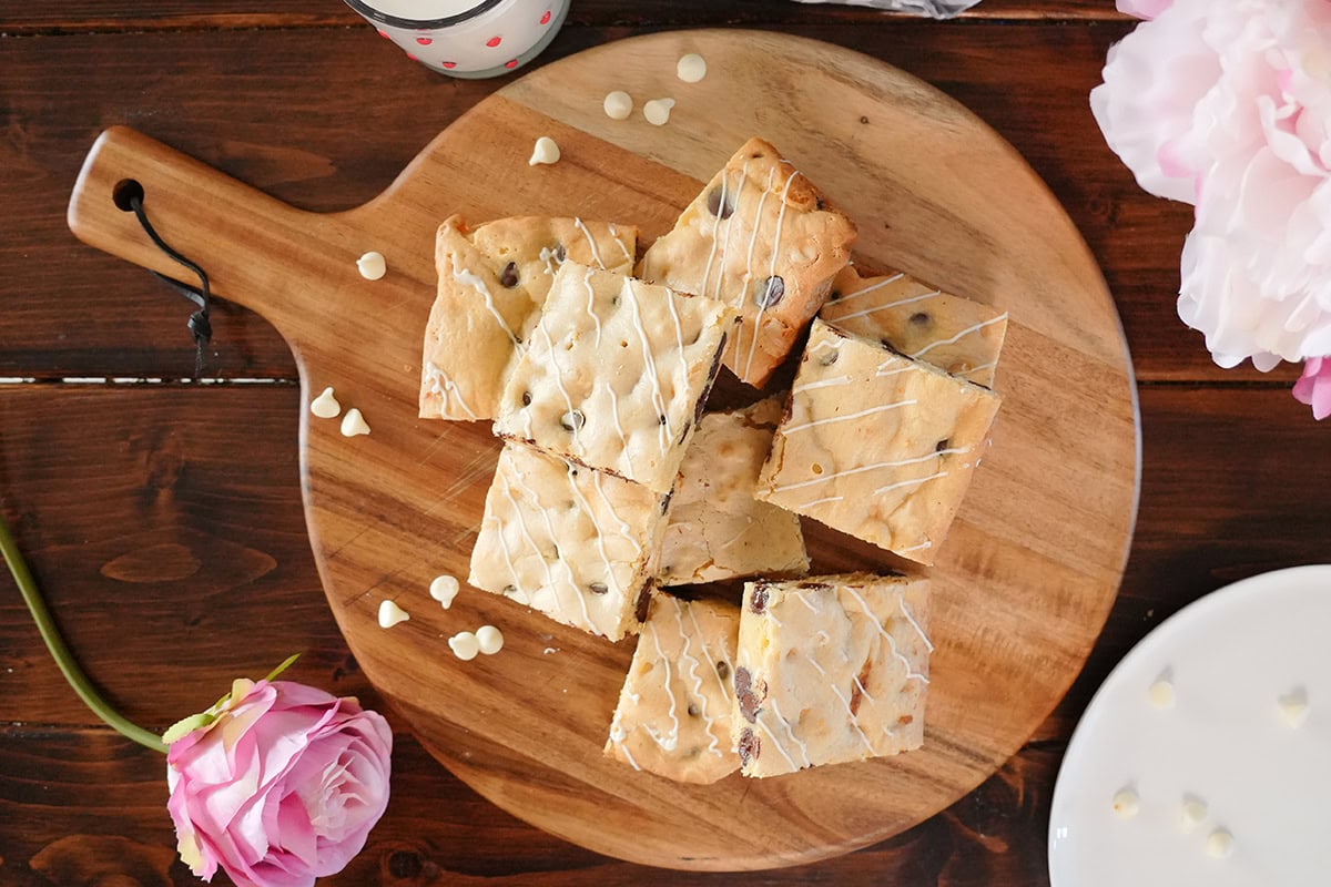 A stack of white chocolate brownies on a wooden cutting board drizzled with white chocolate.  