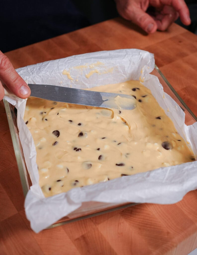 The brownie batter poured in a prepared 8x8 baking dish with parchment paper. 