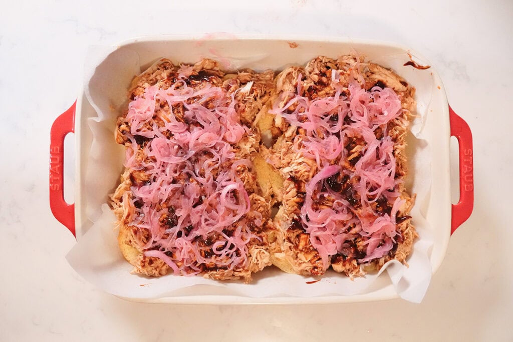 Pickled onions spread on top of chicken on bottom buns.