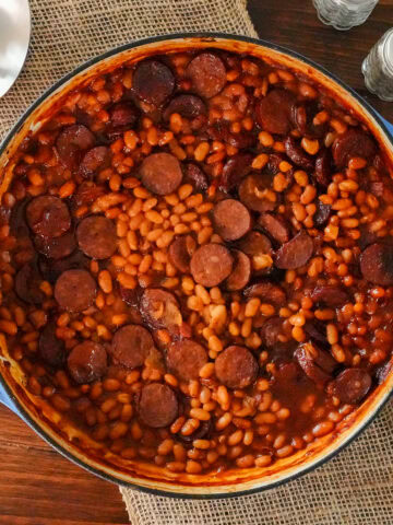 Baked beans and sausage in a skillet with a spoon.