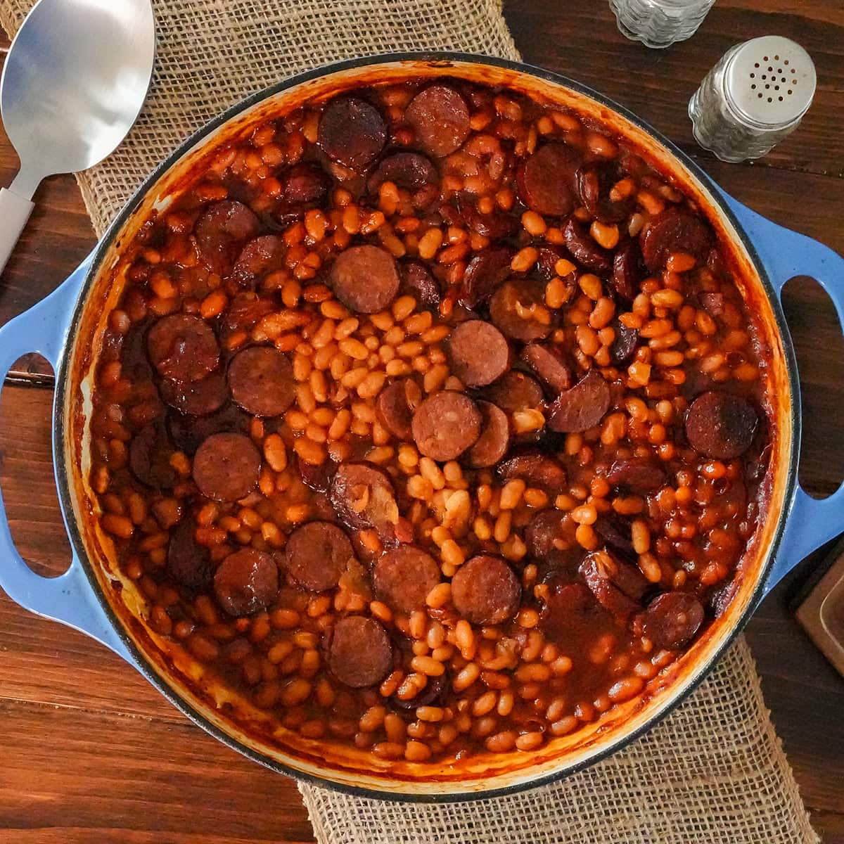 Baked beans and sausage in a skillet with a spoon.
