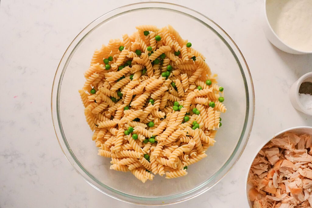 Drained pasta with frozen peas in a glass bowl.