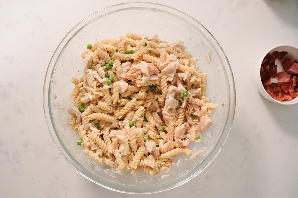 Pasta mixed with chicken, peas and ranch in a glass bowl.