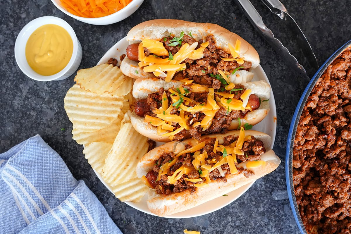 A top view of three chili cheese dogs served with chips. 