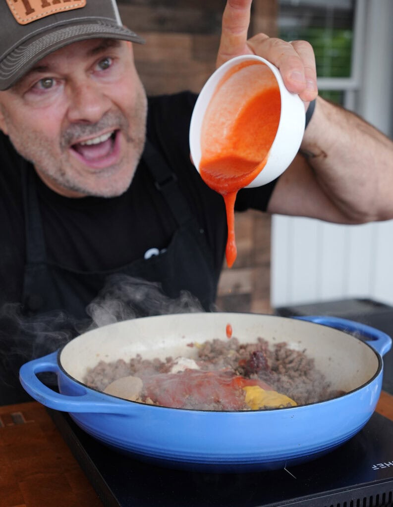 Tim adding tomato sauce and all ingriedints to chili. 
