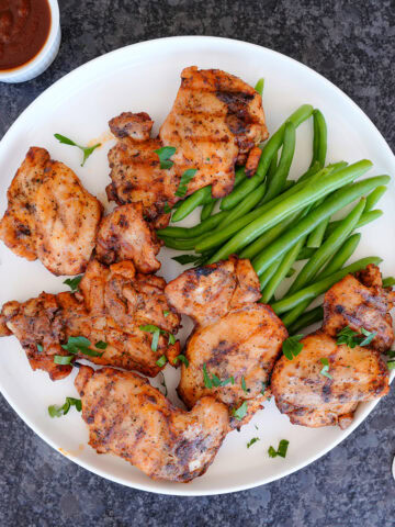 Grilled chicken thighs on a plate with green beans and sauce.