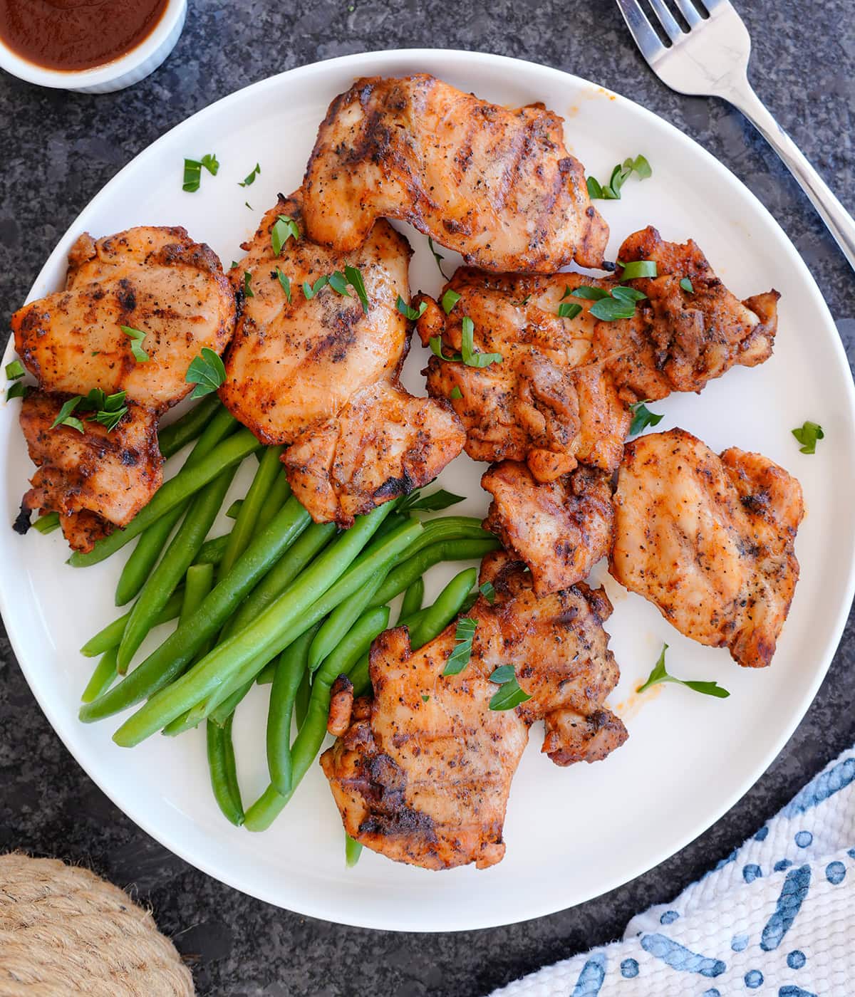 A plate of boneless grilled chicken thighs with green beans. 