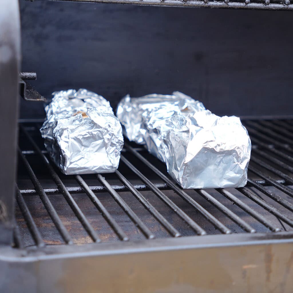 A grill with 4 foil wrapped s'mores.
