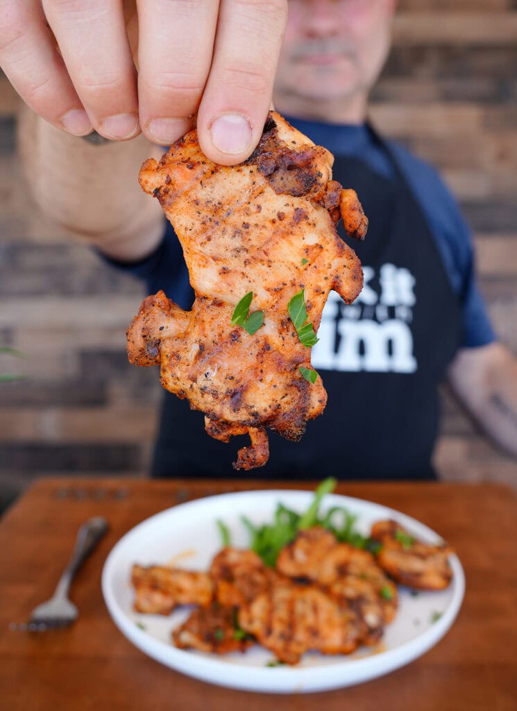 Tim holding up a grilled chicken thigh.
