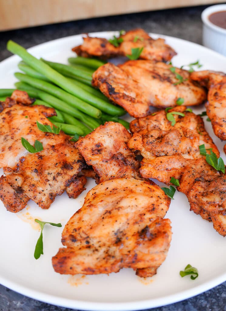 chicken thighs on a plate with parsley and green beans.