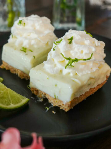 Key Lime Bars on a plate with a lime wedge and whip cream.