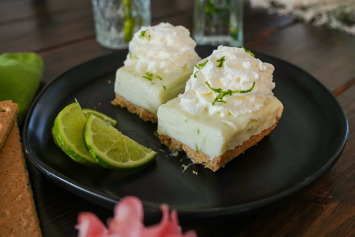 The finished key lime pie bars on a black plate with lime slices. 