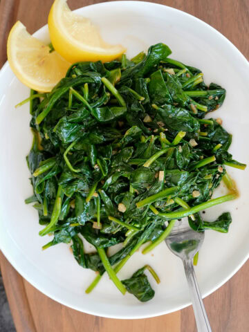 Sautéed spinach on a plate with lemon and a fork.