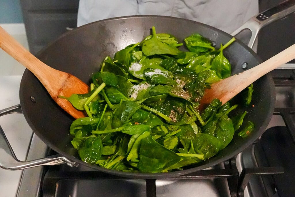 Spinach in a wok with salt and pepper.