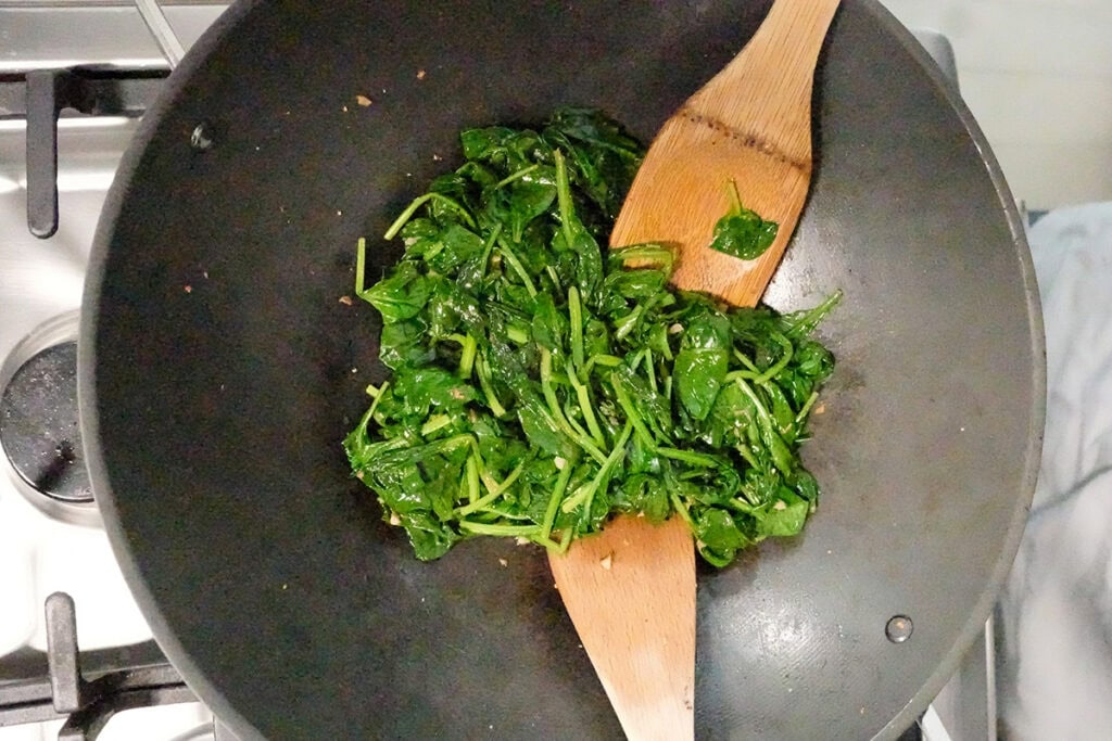 sautéed and wilted spinach with two wooden spoons.