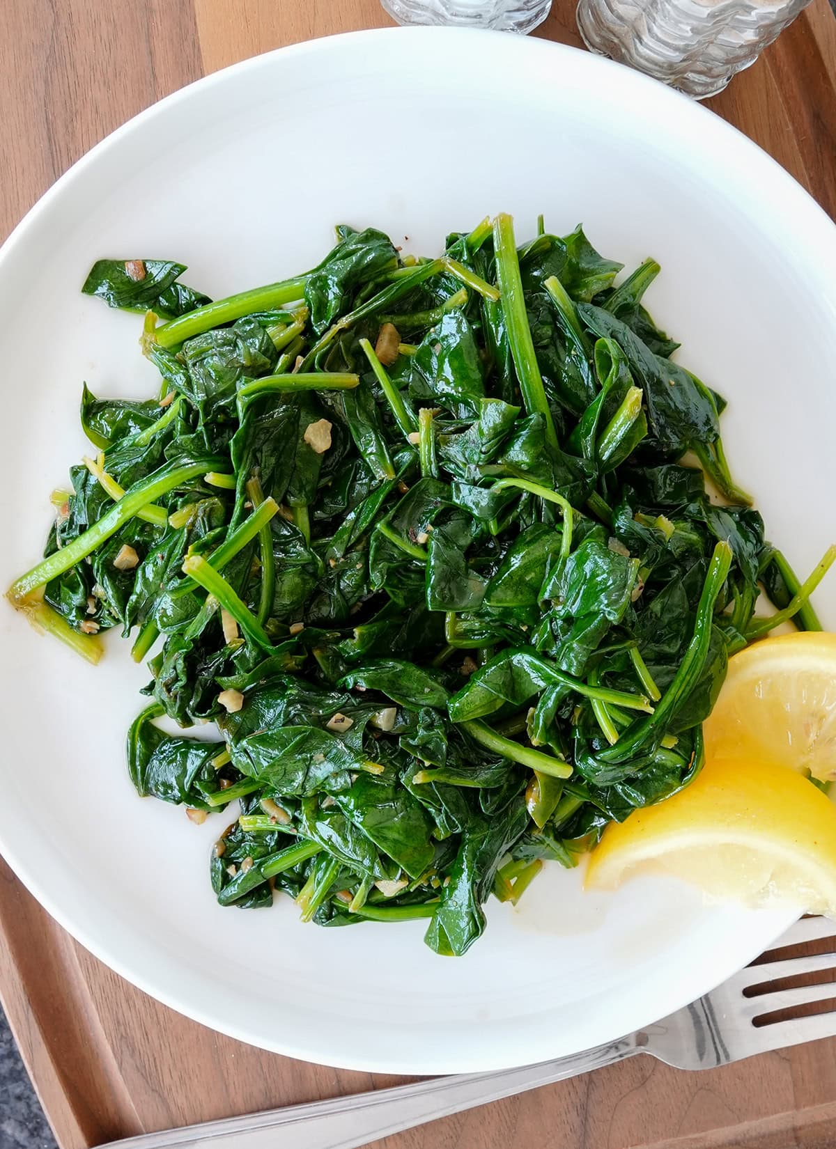 Bright green sautéed spinach on a plate with lemons.