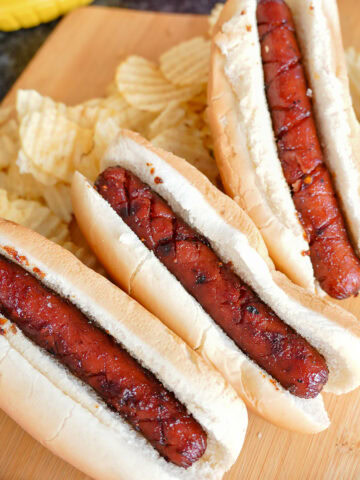 smoked hot dogs in buns next to potato chips.