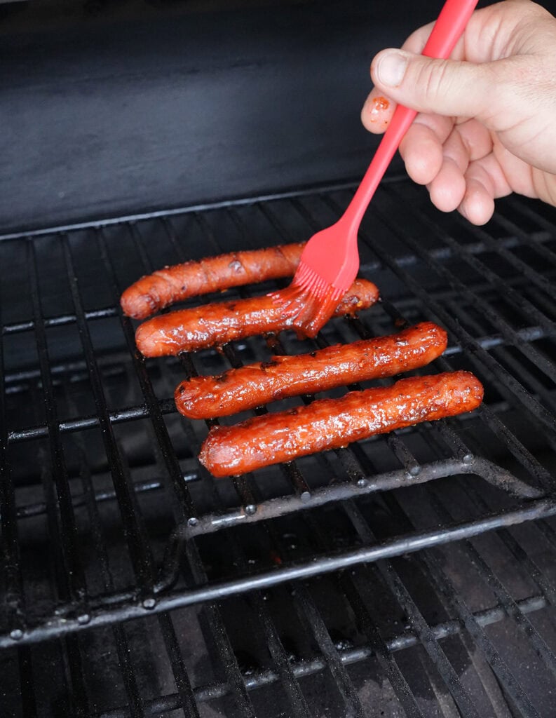 smoked hot dogs being basted with bbq sauce.