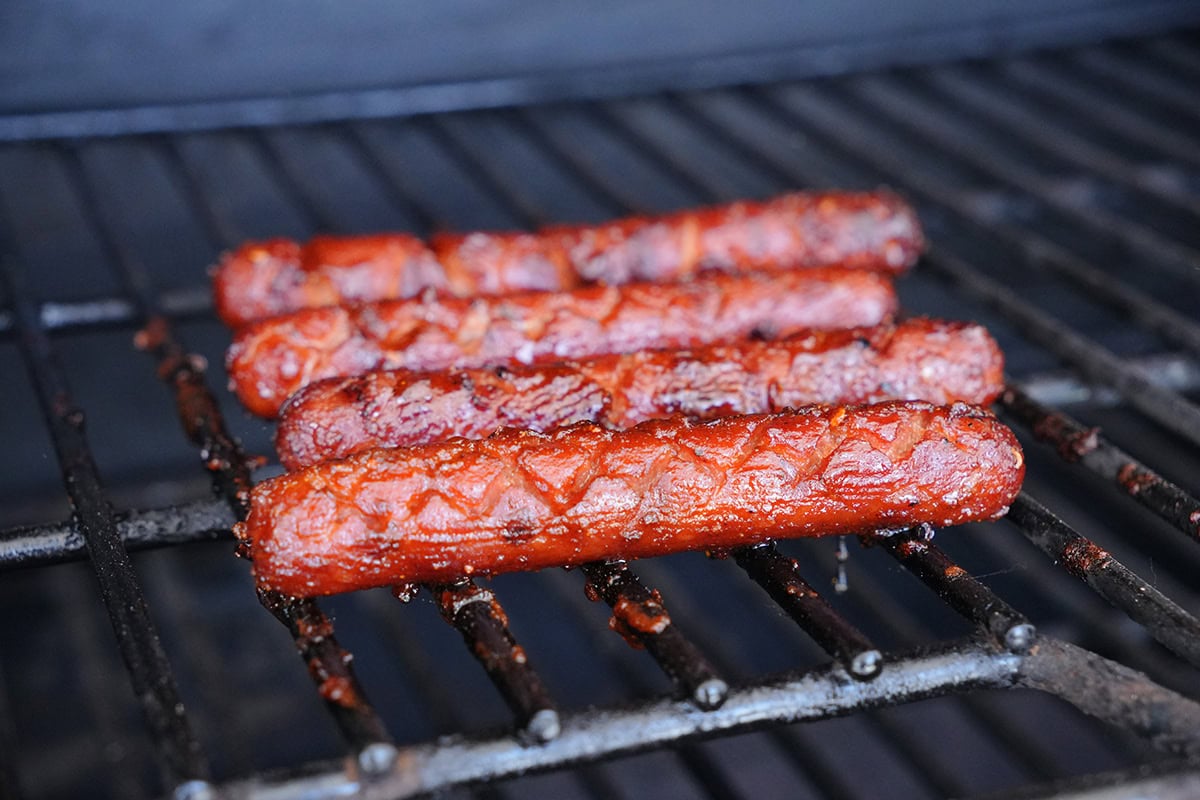 4 smoked hot dogs on grill grates.