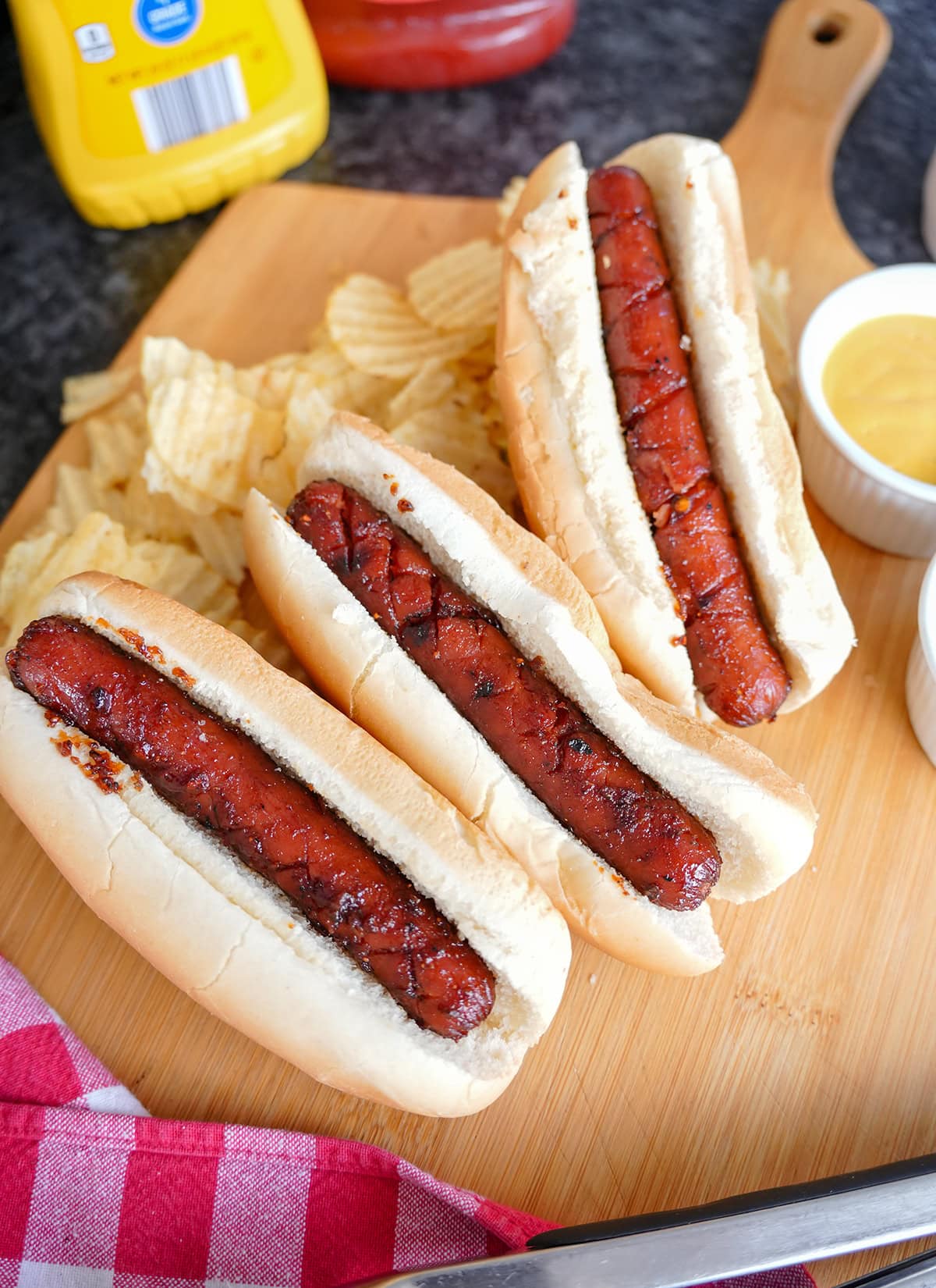 Smoked hot dogs in buns on a platter with chips.