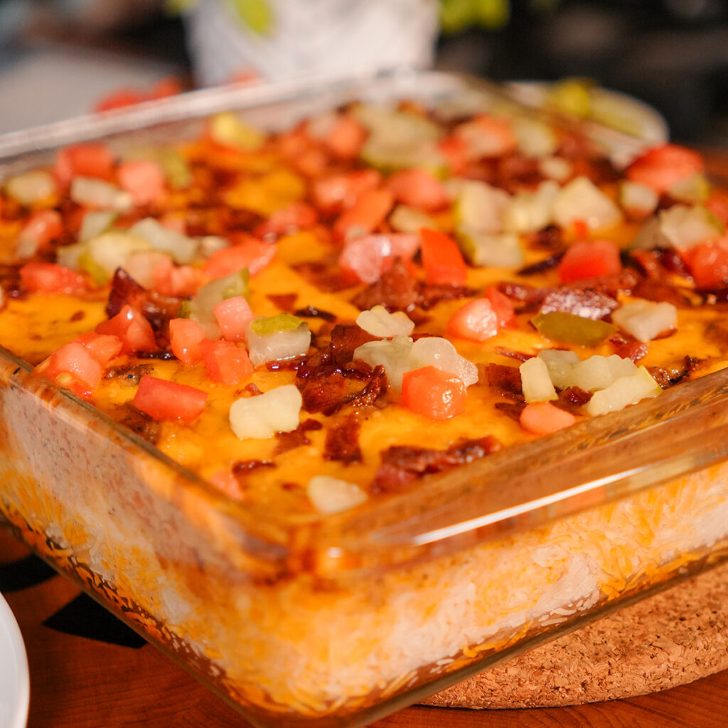 bacon cheeseburger casserole topped with pickles and tomatoes.
