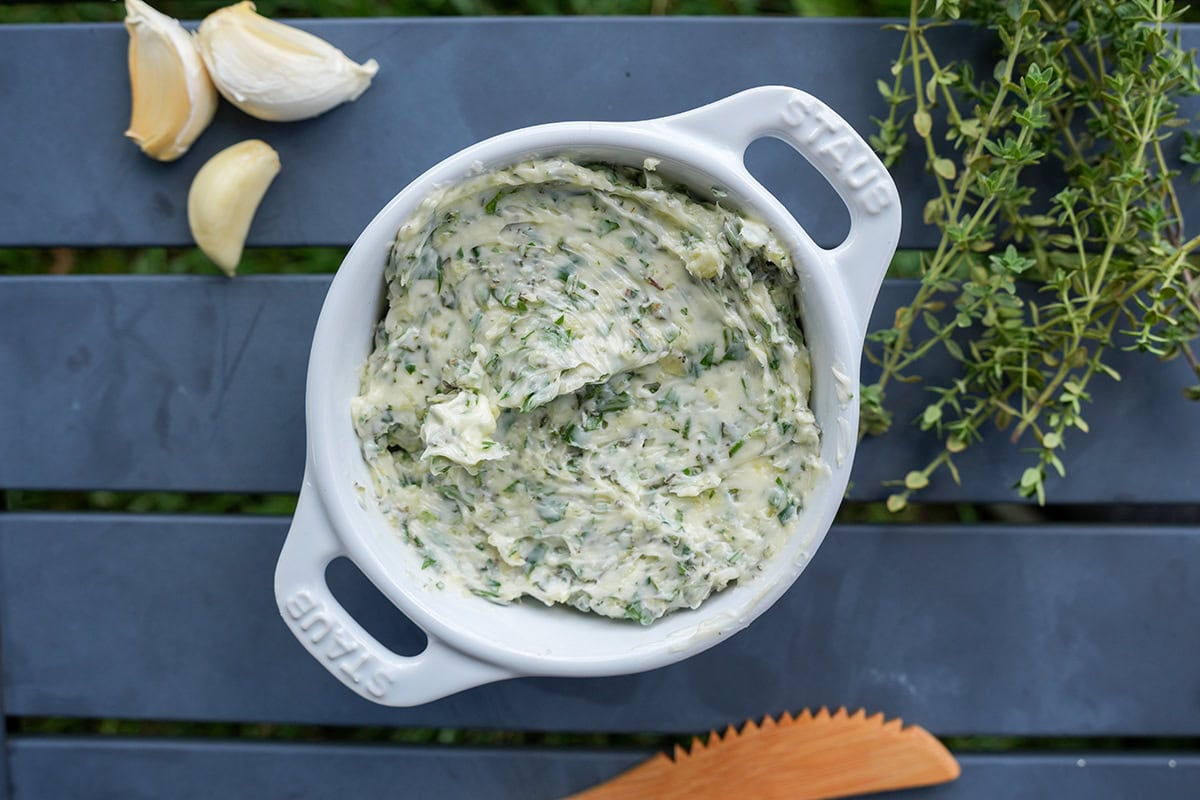 A butter compound in a white dish by herbs.