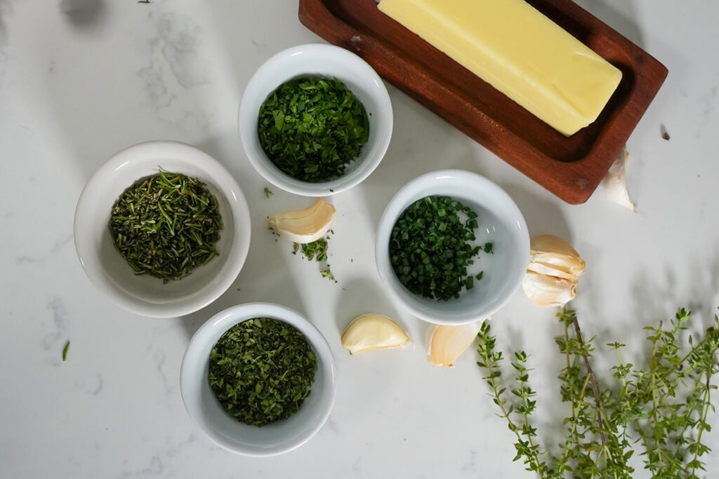 chopped up herbs in bowls next to butter.