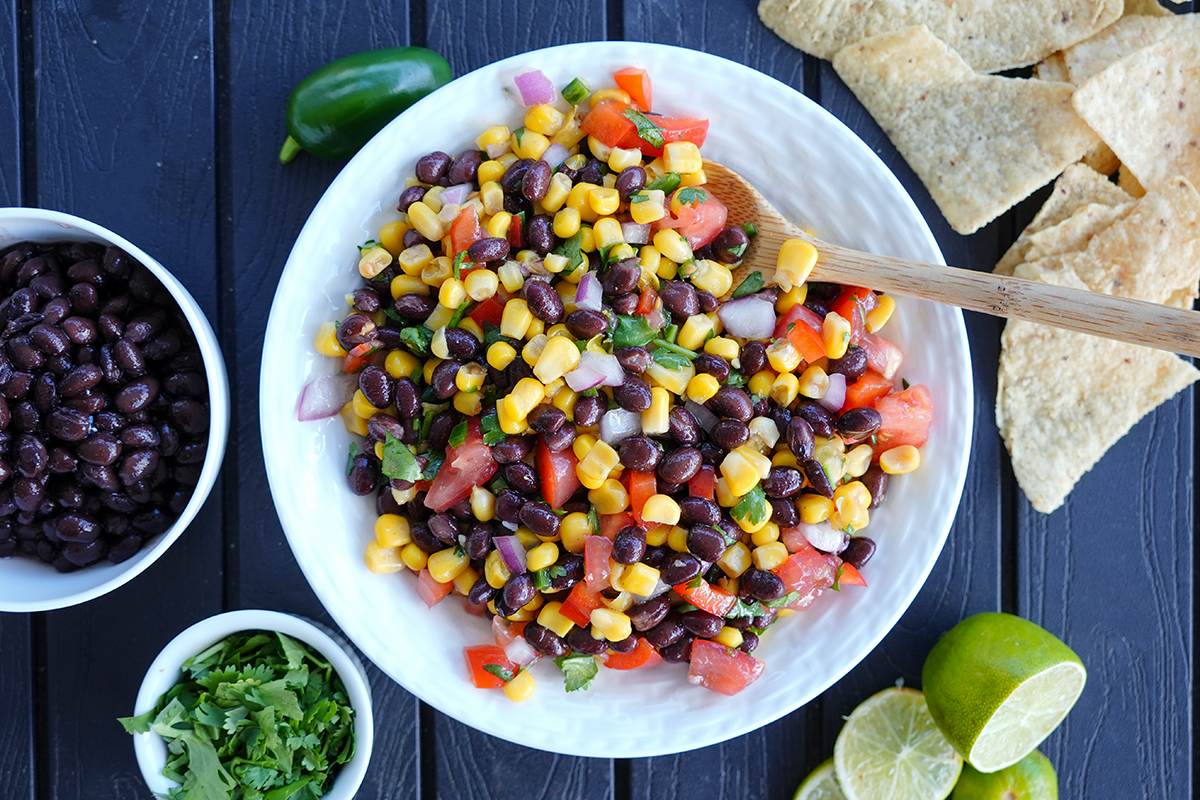 corn salsa in a white bowl next to black beans and limes.