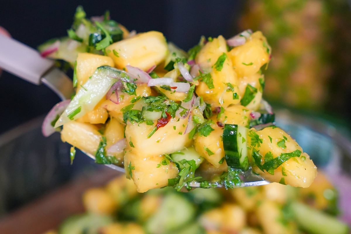 A scoop of pineapples and cucumbers with cilantro and onion.