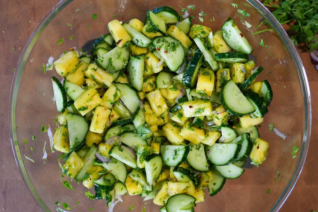A glass bowl of mixed cucumber and pineapples.