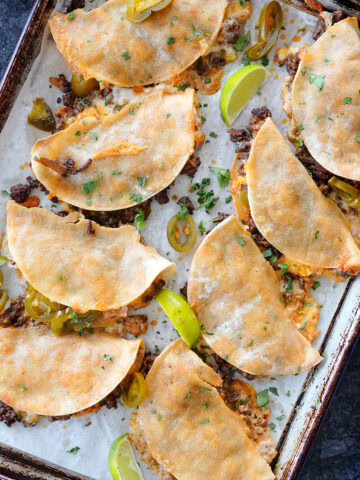 Baked tacos on a cooking sheet with limes and cilantro.