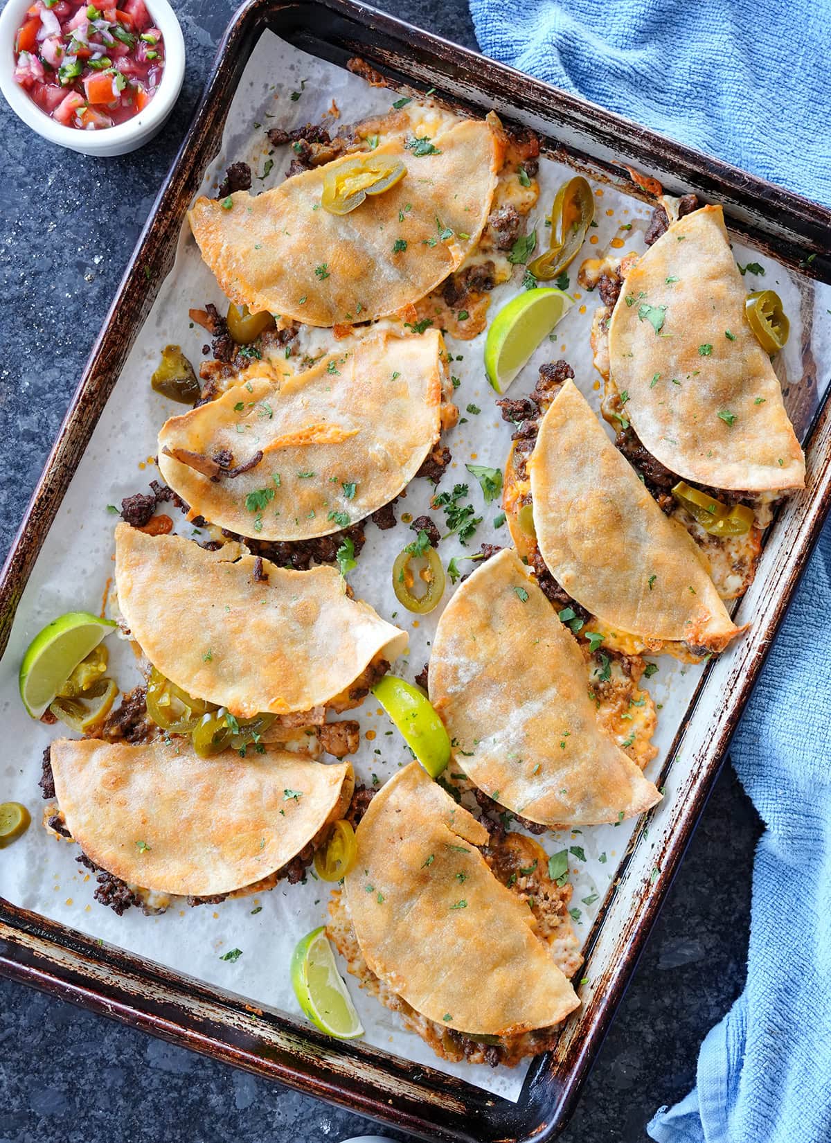 ground beef tacos on a baking sheet with cilantro limes and jalapeños.