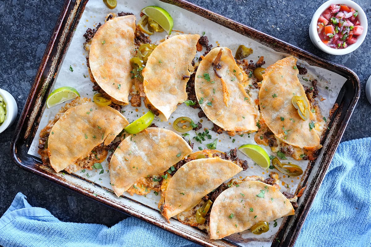 baked tacos on a baking sheet served with limes and salsa.