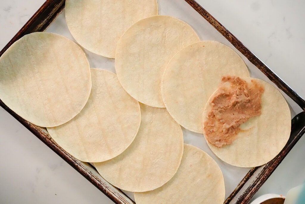 corn tortillas with refried beans on one half of the tortillas.