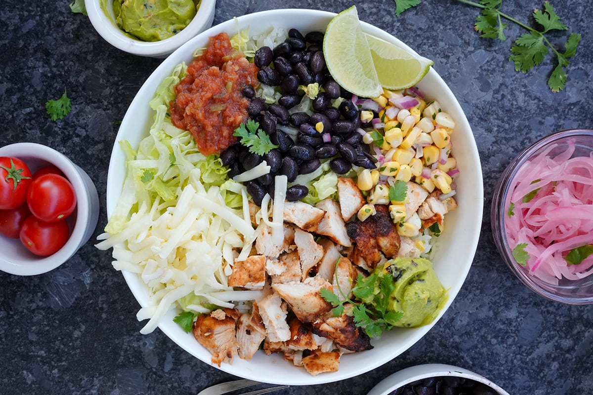 Chipotle chicken burrito bowl with other toppings in small bowls around it.