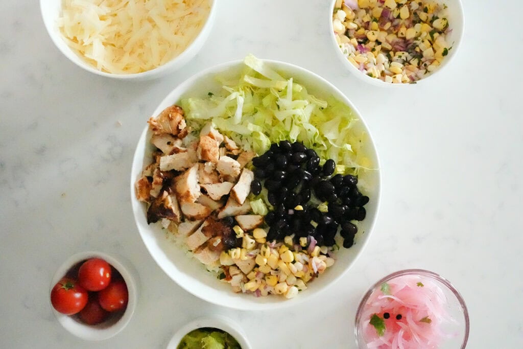 Overhead image of building the chipotle chicken bowl with other toppings in small bowls.