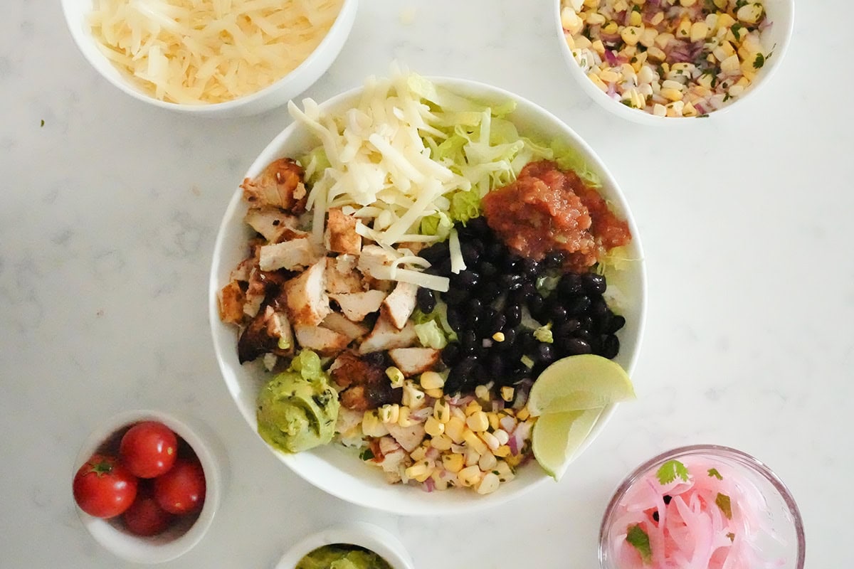 Overhead image of chipotle chicken burrito bowl with other toppings around it.