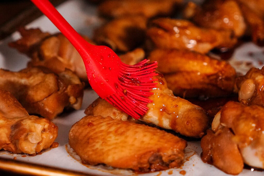 chicken wings being brushed with a teriyaki glaze.