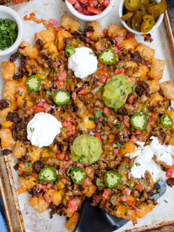 tochos tater tot nachos on a baking sheet with toppings.