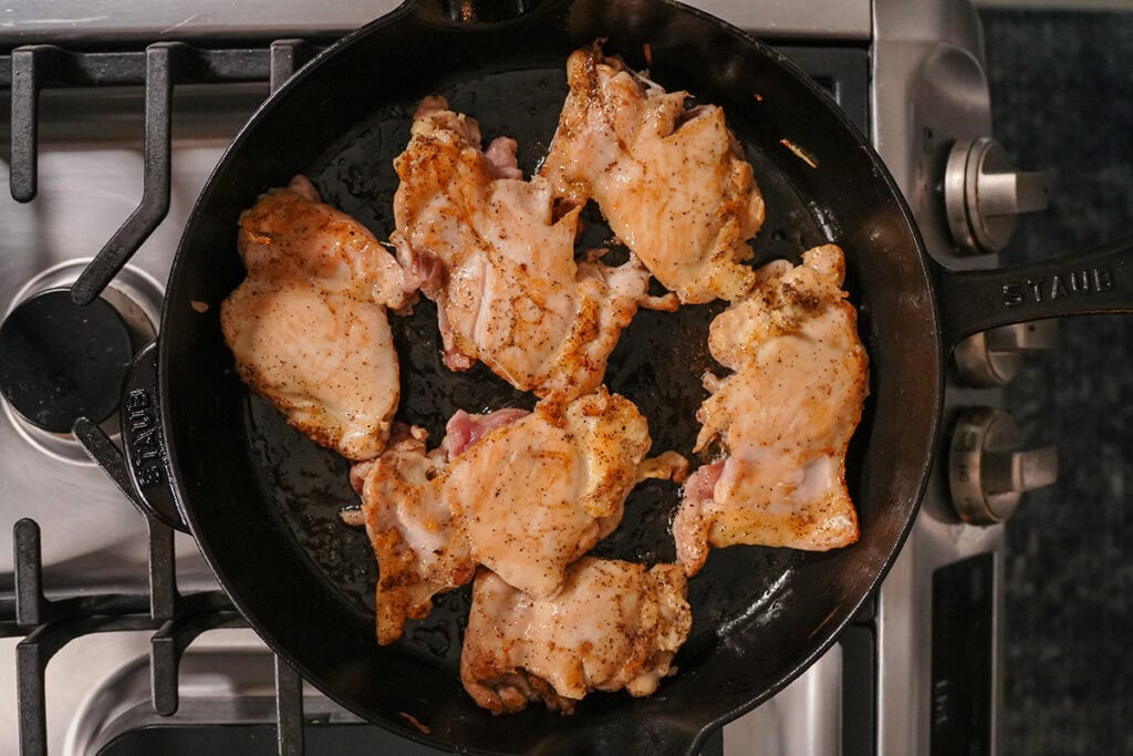 chicken thighs searing in a skillet.